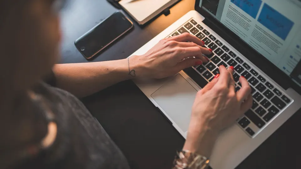Mãos digitando em um notebook com um projeto de página na tela