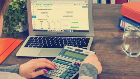Pessoa usando calculadora ao lado de um notebook, fazendo contas de investimento