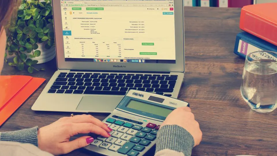 Pessoa usando calculadora ao lado de um notebook, fazendo contas de investimento
